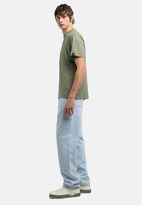 Camiseta verde oliva de manga corta, combinada con jeans holgados azul claro y zapatillas de crema. Diseño simple con un ajuste relajado.