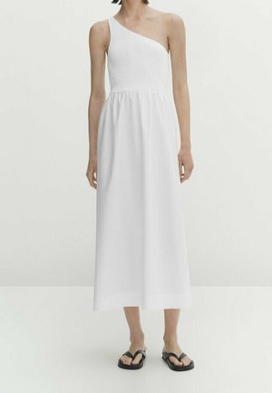 Woman wearing a white one-shoulder midi dress with a fitted, textured bodice and loose skirt, paired with black open-toe sandals.