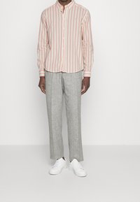 Camisa de hombre de manga larga con rayas verticales rojas y blancas; combinada con pantalones gris claro y zapatillas blancas. Diseño de cuello abotonado.