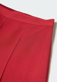 Jupe rouge avec une taille haute et un détail de pli subtil sur un fond clair.