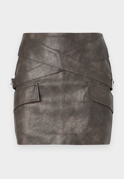 Sötétszürke műbőr mini szoknya aszimmetrikus kialakítással, keresztbe húzódó részletekkel és oldalsó zsebekkel, fémes díszítéssel.