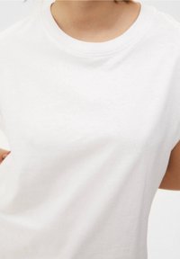 Witte katoenen T-shirt met een ronde halslijn en korte mouwen. Hete zachte textuur, eenvoudig ontwerp zonder zichtbare patronen of accenten.