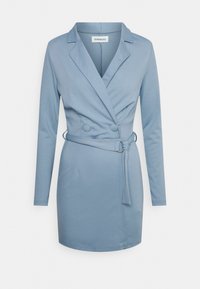 Vaaleansinisestä pehmeästä kankaasta valmistettu blazer-dressi, jossa on pitkät hihat, lovettu kaulus, kaksinkertaiset napit ja sidottu vyötärövyö.