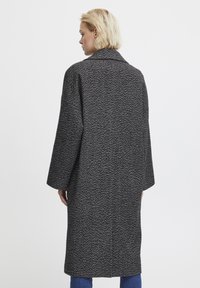 Cappotto lungo a righe herringbone bianco e nero con ampi revers, spalle scese e vestibilità morbida. Textura liscia, lunghezza al ginocchio con tasche laterali.