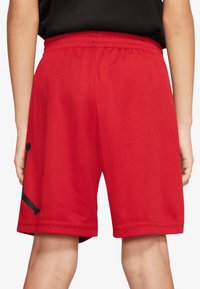 Czerwone sportowe szorty z siateczki z elastycznym paskiem w talii. Na lewej nogawce czarne logo, luźny krój. Gładka faktura, długość do kolan.
