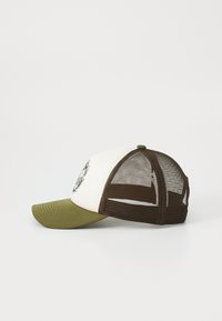 Gorra de camionero con panel frontal blanco, visera verde oliva y parte trasera de malla marrón. Presenta un diseño gráfico circular en la parte delantera.
