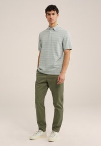 Camisa polo de manga corta para hombre en verde claro con rayas horizontales. Combinada con pantalones verdes oliva y zapatillas blancas.