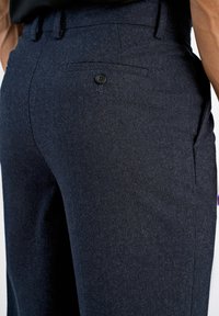 Calças azul-marinho feitas de um tecido texturizado, com um bolso traseiro com um botão preto e um design de perna reta.