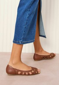Ballerines en cuir marron avec un design découpé et un bout ouvert, associées à un jean en denim cropped avec un ourlet effiloché.