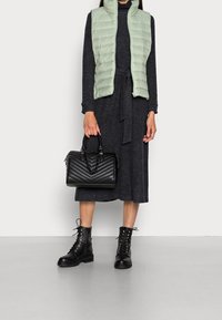 Gilet imbottito verde chiaro, vestito lungo grigio scuro con cintura in vita, borsa a tracolla nera trapuntata e stivali alla caviglia neri con lacci.