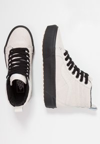 Hohe Sneakers aus weißem Wildleder mit schwarzen Schnürsenkeln, schwarzer Gummisohle und texturiertem Gummiprofil. Mit Logo auf der Zunge und glatten Akzenten.