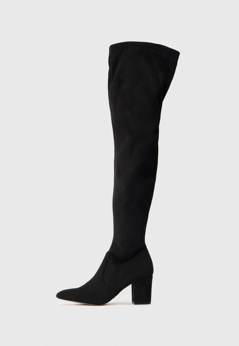 Botte noire en daim au-dessus du genou avec bout pointu et talon carré sur un fond clair uni.