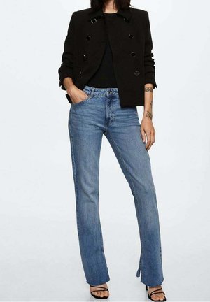 Zwarte dubbelgevoerde blazer met grote knopen, gecombineerd met lichtblauwe flared jeans met zijsplits aan de zoom.