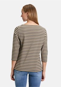 Beige gestreiftes Langarmshirt mit schwarzen horizontalen Streifen, Bootsausschnitt und Dreiviertelärmel, kombiniert mit hellblauen Jeans.