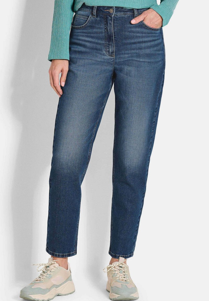 Jeans en denim bleu foncé avec une taille haute, une coupe droite, des poches avant et une fermeture à boutons, associés à des baskets claires.