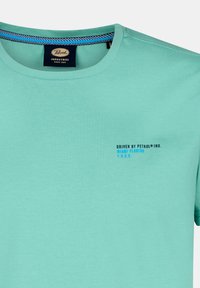 Svetlo tyrkysové tričko s krátkym rukávom vyrobené z jemnej bavlny, s okrúhlym výstrihom a malým modrým textom "DRIVEN BY PETROL® IND. MIAMI FLORIDA 1.9.9.3".