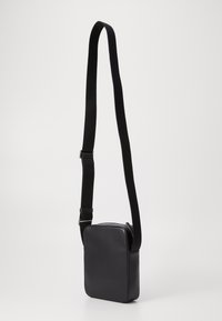 Bolso negro de hombro hecho de cuero suave, que presenta una forma rectangular y una correa larga y ajustable para un uso cómodo.