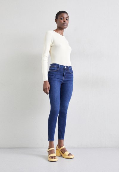 Haut à manches longues crème clair, jeans ajustés bleus et chaussures à plateforme jaunes. Texture lisse, coupe cintrée et design minimaliste.
