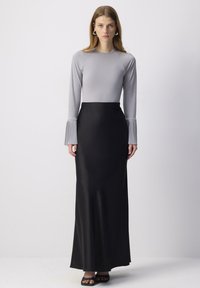 Top gri cu mâneci lungi și manșete plisate, asortat cu o fustă maxi neagră elegantă. Materialul pare neted și mulat, evidențiind forma corpului.