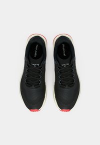 Baskets de course noires avec une tige texturée, des accents rouges et une semelle blanche. Présente des lacets plats et un logo sur la languette et la semelle intérieure.
