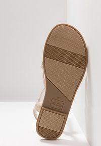 Beige-sandaalit, joissa on teksturoitu kumipohja, matala korko ja kuvioidut yksityiskohdat. Brändi merkitty sivulle. Hihnat ovat kudottua kangasta.