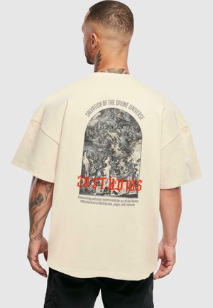 Cremefarvet oversized t-shirt med korte ærmer, der har et grafikdesign på ryggen, som viser detaljeret kunstværk og dristige røde tekstakcenter.