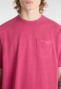 Kurzärmliges T-Shirt mit Rundhalsausschnitt aus lebhaft pinkem Baumwollmaterial, mit einer strukturierten Taschenapplikation auf der linken Seite. Glatte Oberfläche und lockere Passform.