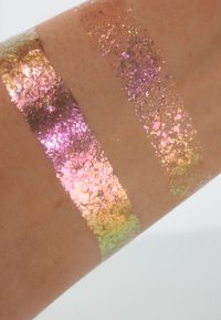 Tre skimrende striper av iriserende glitter på huden: rosa-lilla, gull og grønn. Hver av dem har en fin, teksturert overflate som reflekterer lys.