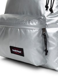 Zaino in nylon argento con texture, dotato di tasca frontale, cerniere nere e patch con logo Eastpak nero. Presenta chiusure a cordino.