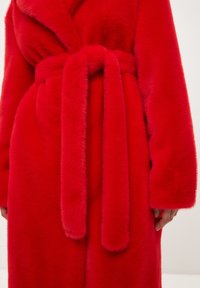 Bata de piel sintética roja con cinturón anudado en la cintura, mangas largas y una textura suave, con un escote en V profundo y tela aterciopelada.