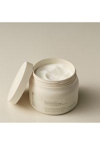 Crème-kleurige pot met een gestructureerd etiket, met de tekst "BONDIFINITY DEEP REPAIR MASK." Deksel deels open, waardoor de witte crème aan de binnenkant zichtbaar is.