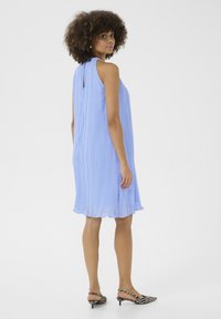 Light blue pleated sleeveless dress with a keyhole back detail, featuring a flowy hem, paired with black and white striped heeled shoes.