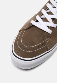 Baskets en daim marron avec des lacets blancs, des coutures contrastantes, un bout arrondi et une semelle en caoutchouc blanche texturée avec un accent noir.