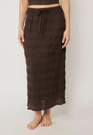 Frau barfuß, trägt einen dunkelbraunen, texturierten Midirock mit Kordelzug in der Taille und ein passendes kurzes Top.