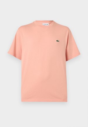 T-shirt Lacoste rose clair à manches courtes, col rond, avec petit logo crocodile vert sur la poitrine gauche.