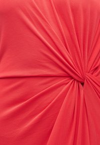 Κόκκινο ύφασμα διπλωμένο σε κόμπο, δημιουργώντας ακτινωτές πτυχώσεις και λεπτομέρειες υφής.