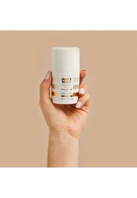 Bottiglia cilindrica bianca tenuta in mano, etichettata "James Read Gradual Tan Deep Mask Tan Face", con dettagli dorati e un tappo a vite.