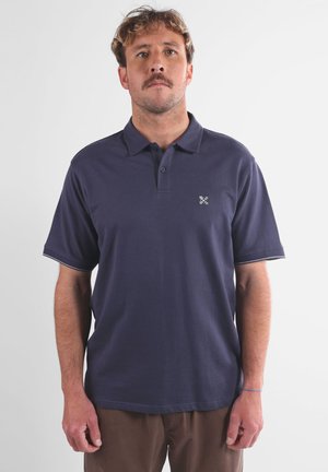 Polo en bleu marine en coton. Manches courtes avec un col à boutons. Présente un petit logo brodé sur la poitrine gauche.