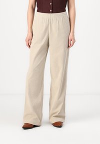 Pantaloni beige in corduroy a gamba larga con cintura elastica, caratterizzati da una texture a righe verticali e una vestibilità rilassata, abbinati a scarpe marroni a punta.