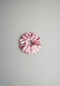 Rózsaszín és fehér csíkos szövet hajgumi, redős textúrával, kör alakú és sima felülettel, világosszürke háttéren elhelyezve.