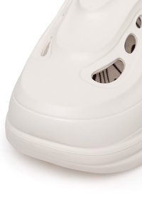 Pantofii sintetici albi cu vârf rotunjit, orificii de ventilație laterale, fuselaj texturat și un design minimalist. Finisaj neted cu o ușoară strălucire.