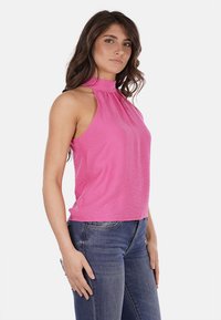 Top senza maniche di colore rosa, con collo alto, realizzato in tessuto leggero e dalla morbida texture. Abbinato a jeans blu, con una vestibilità comoda.