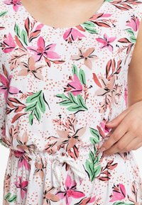 Floweri printti mekko, jossa on vaaleanpunaisia, vihreitä ja beigejä kukkia valkoisella taustalla. Mekossa on pyöreä kaula-aukko ja joustava nyöri vyötäröllä.