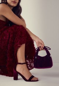 Sandale cu toc înalt din catifea burgundy, cu o bandă lată și curea la gleznă, asortate cu o geantă mică în aceeași nuanță, prevăzută cu mânere în formă de fundă.