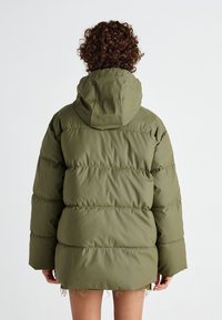 Doudoune vert olive avec capuche, présentant des sections matelassées et une coupe décontractée. Le tissu semble lisse et légèrement brillant.