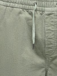 Gros plan de la taille d'un pantalon en velours côtelé vert clair avec cordon de serrage et embout métallique à l'extrémité du cordon.