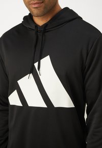 Sweatshirt preto com capuz e um grande logo branco de três riscas no peito. Feito de tecido suave, possui capuz com cordão e bolso tipo canguru.