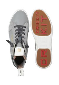 Grijze hoge sneakers van suede en leer, met zwarte veters, een witte zool en rode "CRICKIT" branding op de loopzool.