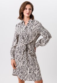 Robe en imprimé zèbre noir et blanc en tissu léger, avec un devant à boutons, des manches longues et un détail à la taille noué.
