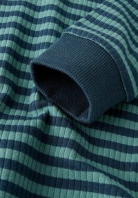 Zbliżenie na żebrowany materiał o ciemnozielonych i granatowych poziomych paskach oraz granatowym mankiecie.